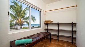 Quarto com um banco, prateleira com toalhas e janela com vista para palmeiras e o oceano.