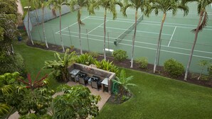 A tennis court surrounded by palm trees and a barbecue area with a view of the court.