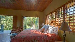 A bedroom with a bed, a nightstand, a chair, and a view of the outdoors.