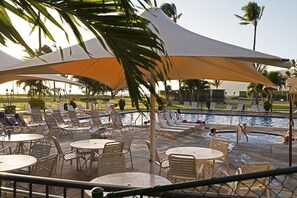 Zona piscina con sedie a sdraio, tavolini e ombrelloni.