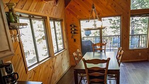 A wooden cabin interior with a dining area, kitchen, and large windows.