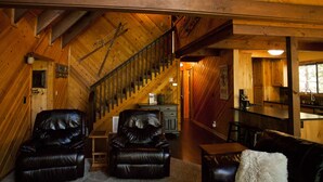 A cozy attic bedroom with a sloped ceiling, wooden beams, a staircase, a kitchenette, and leather furniture.