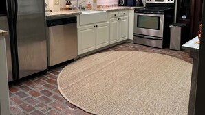 A kitchen with white cabinets, stainless steel appliances, a brick floor, and a round rug. - Charming 2 bedroom condo in the heart of beautiful Natchez, MS. (Natchez)