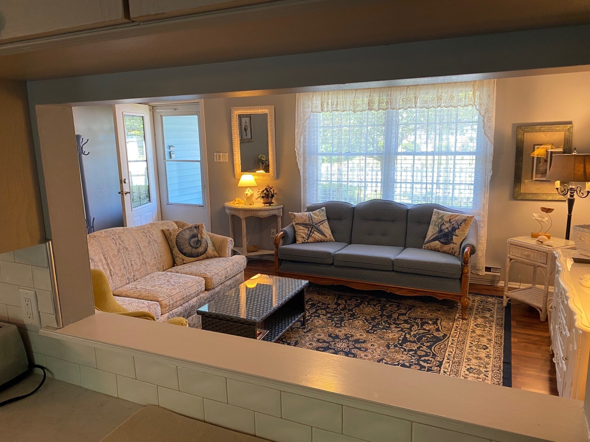 A living room with two sofas, a coffee table, a patterned rug, and a window with lace curtains.