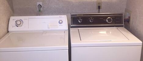 A laundry room with two white washing machines and a dryer, wooden cabinets above, and a countertop with a power outlet.