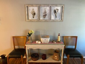 A dining area with a table set for two, featuring a lace tablecloth, a pitcher of flowers, a lighthouse ornament, and a basket.