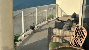 A balcony with wicker furniture, a glass table, and a view of the ocean.