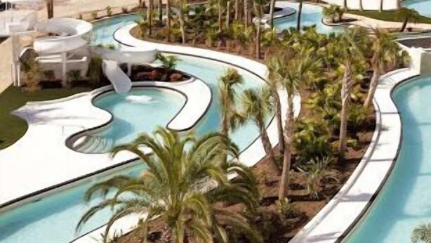 A pool area with multiple water features, palm trees, and a beach view.