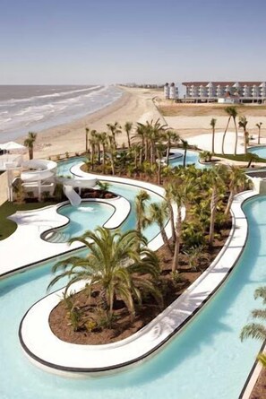 A pool area with multiple water features, palm trees, and a beach view.