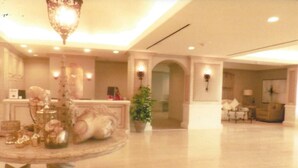 A spacious lobby with a marble floor, a round table with decorative items, a chandelier, and a seating area with a sofa and armchairs.