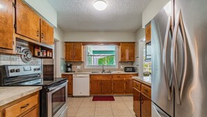 A kitchen with wooden cabinets, a stainless steel refrigerator, a dishwasher, and a window with a view of greenery. - Siesta beach....one and only (Sarasota)