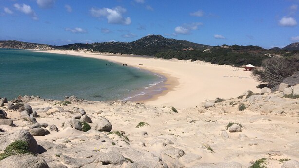 Ein Strand mit klarem türkisblauem Wasser, sandigem Ufer und Felsenformationen.