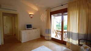 Ein Schlafzimmer mit einem Bett, einem Fernseher auf einer Kommode, einer Schiebetür zu einem Balkon und einem Deckenventilator.