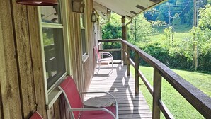 A wooden deck with red and white chairs, a railing, and a view of a green landscape.