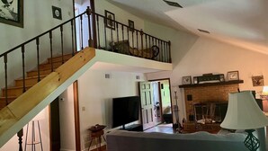 A spacious living area with a wooden staircase, a fireplace, and a television.