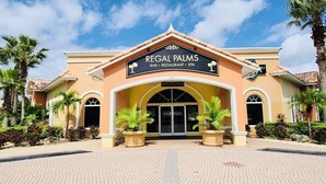 Un edificio con un cartel que dice "Regal Palms Bar, Restaurant, Spa" y una amplia entrada con palmeras frente a él.