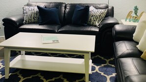 Una sala de estar con un sofá de cuero negro, una mesa de centro blanca y un tapete estampado.
