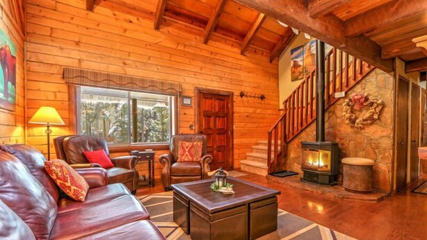 Interior acogedor de una cabaña de troncos con un sofá de cuero, una chimenea y una escalera que sube a una buhardilla.