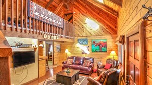 Un interior de cabaña acogedor con paredes de madera, una chimenea, un sofá y un televisor.