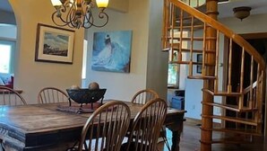 Un espace repas avec une table et des chaises en bois, un lustre et un escalier en colimaçon.