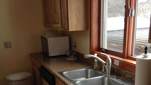 Una cocina con armarios de madera, un lavamanos de acero inoxidable y una ventana con vistas al exterior.