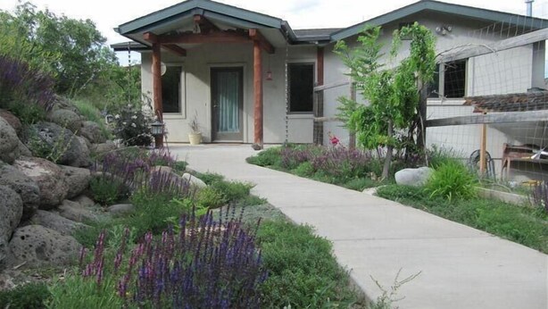 Una casa con porche cubierto, un camino de concreto y un jardín con diversas plantas.