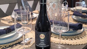 Spisebord dækket med vinglas, en flaske Syrah 2021 og servietter.