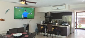 A modern kitchen with a central island, a dining area with a TV, and a ceiling fan.