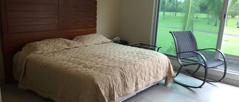Un dormitorio con una cama grande, cabecera de madera, una silla junto a la ventana y vistas a un paisaje verde.