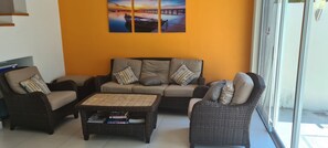 A living room with a sofa, two armchairs, and a coffee table. There is a painting on the wall and a window with a view outside.