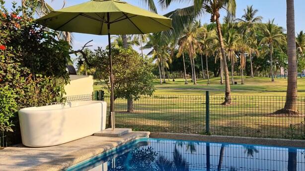 Zona de piscina con una sombrilla verde, una maceta blanca y vistas a un campo de golf con palmeras.