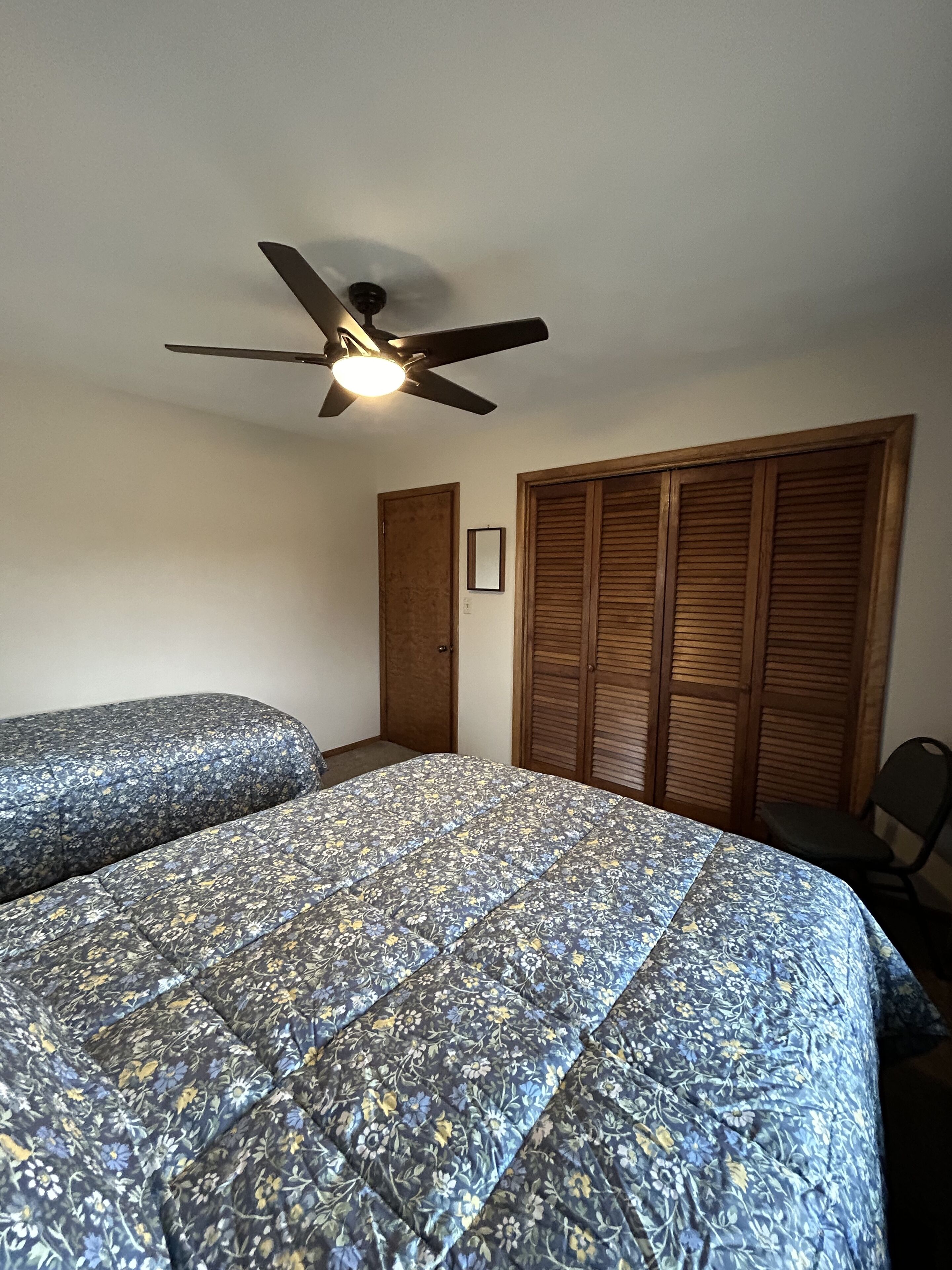Une chambre avec deux lits, un ventilateur de plafond, une armoire et une chaise.