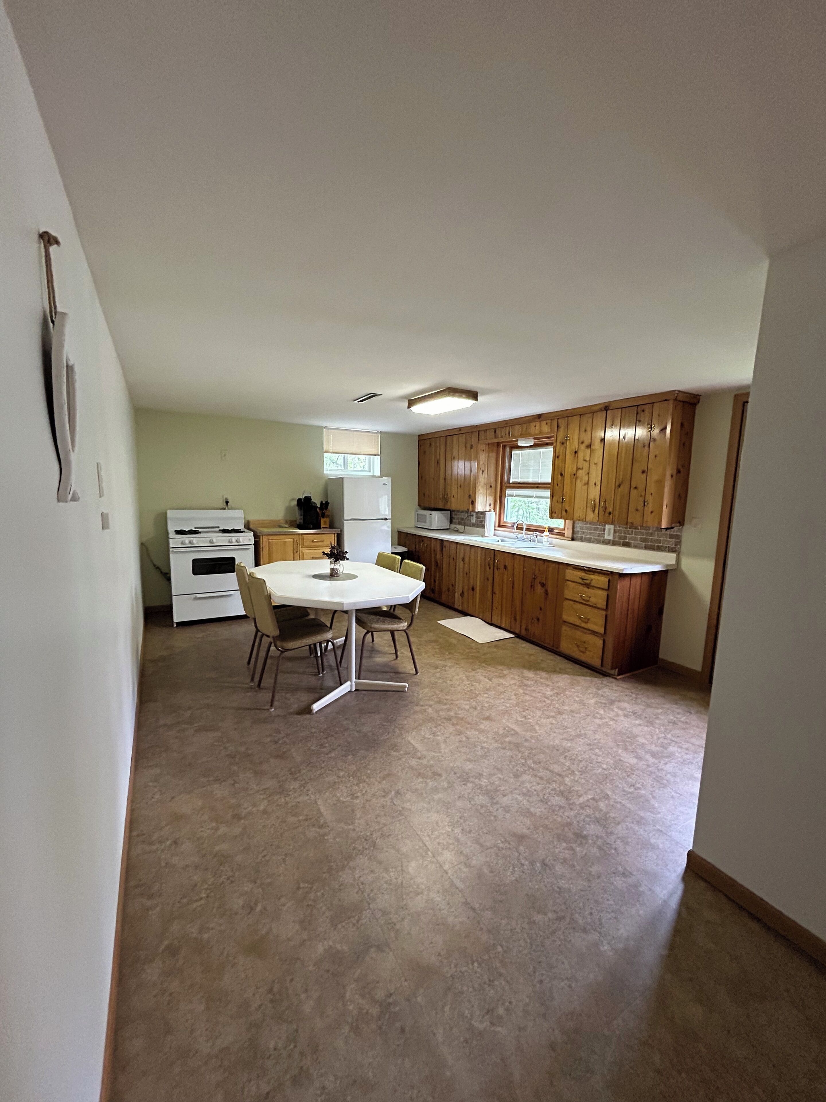 A compact kitchen with wooden cabinets, a white stove, a microwave, and a dining table with chairs.