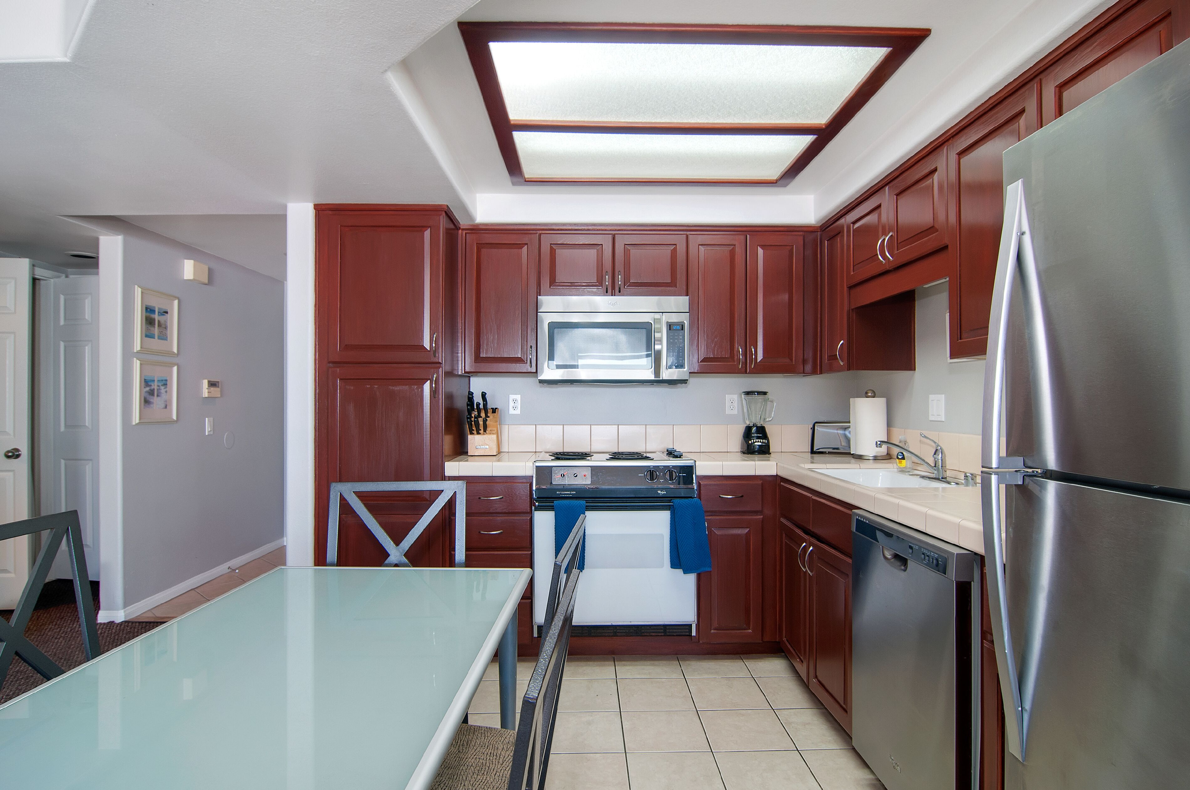 A modern kitchen with wooden cabinets, stainless steel appliances, and a glass dining table.