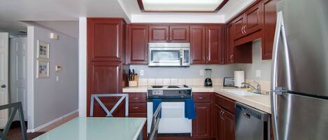 A modern kitchen with wooden cabinets, stainless steel appliances, and a glass dining table.