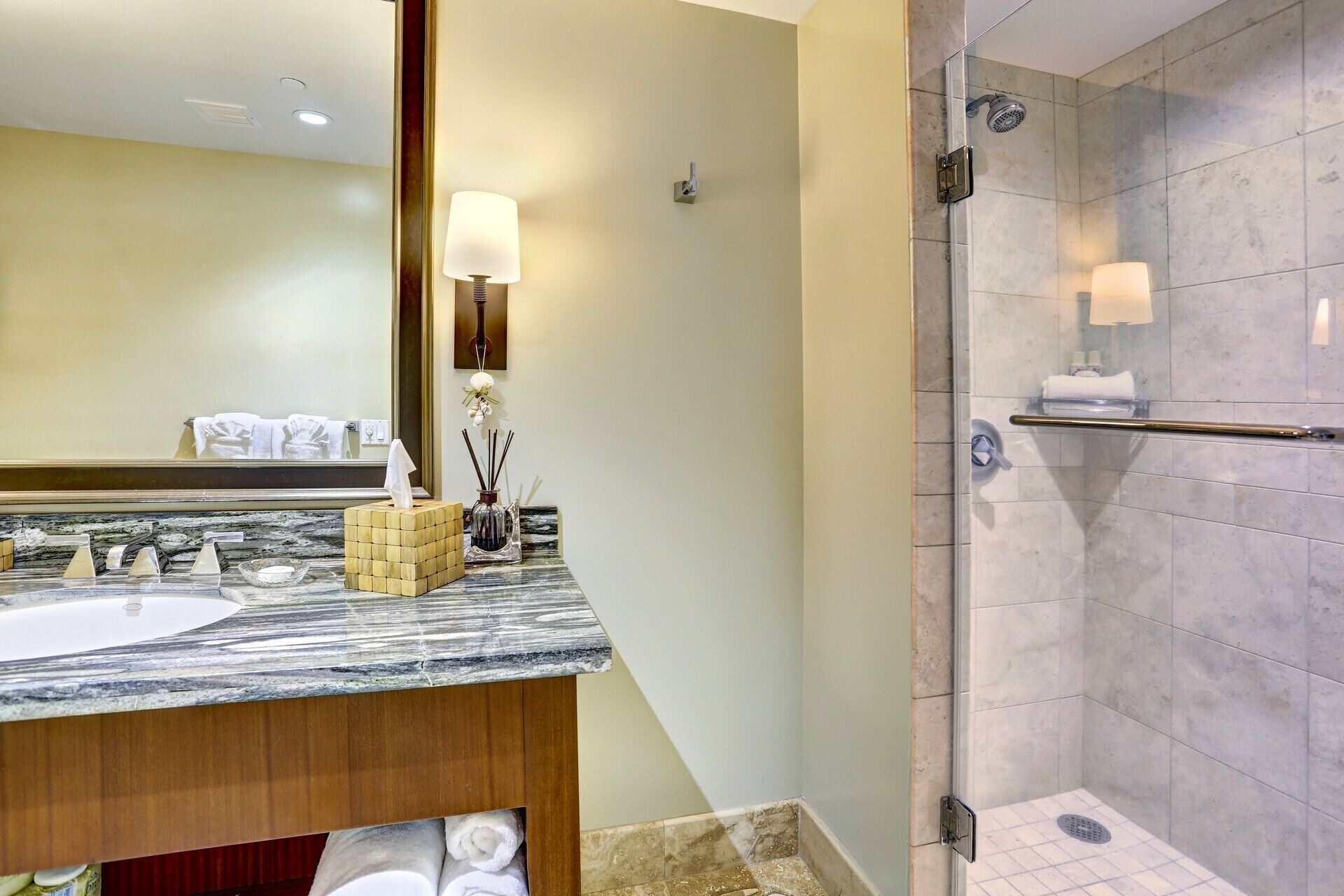 A bathroom with a marble sink, a glass shower enclosure, and a mirror with a wall-mounted lamp.