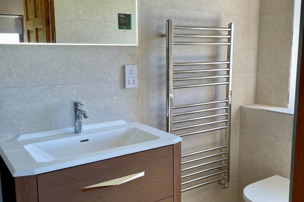 Une salle de bain avec un lavabo blanc, un meuble-lavabo en bois et un porte-serviettes chromé.