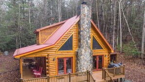 Eine Blockhütte mit einem Steinkamin, einer Holzterrasse und einem überdachten Sitzbereich im Freien.