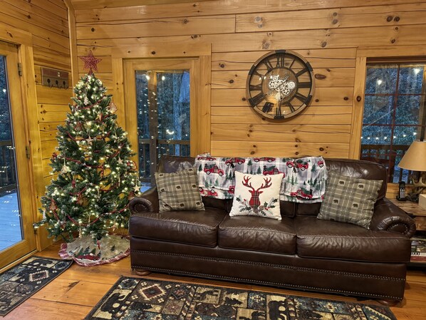 A cozy cabin interior with a Christmas tree, leather sofa, and a large wooden wall clock.