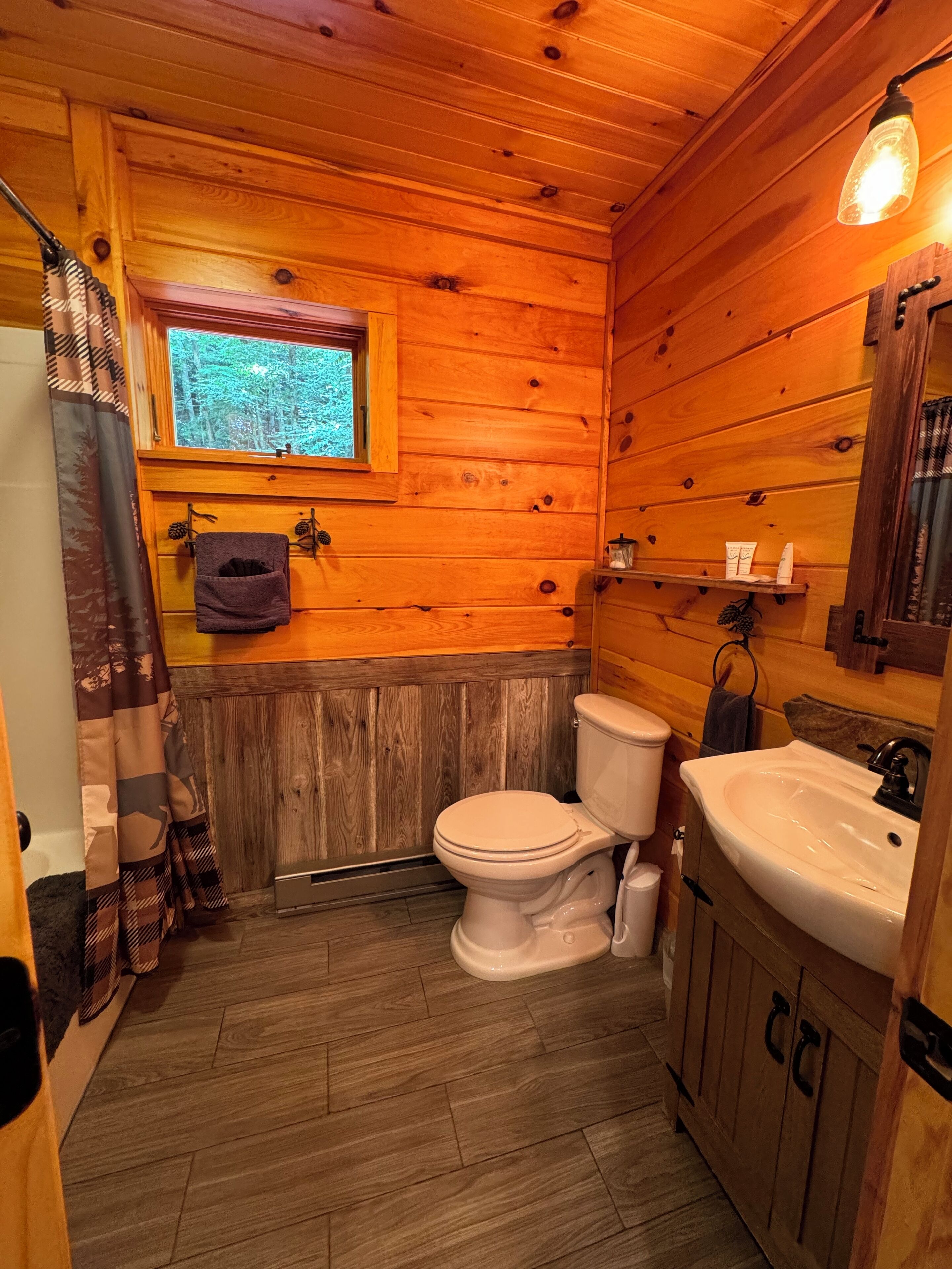 A wooden cabin bathroom with a toilet, sink, and window.