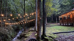 Eine Holzhütte mit einer Holzterrasse und Lichterketten in einer Waldlandschaft.