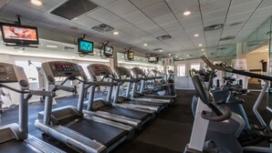 A gym with multiple treadmills, exercise bikes, and a television mounted on the wall.