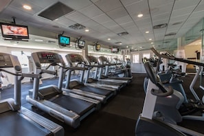 Een fitnessruimte met meerdere loopbanden, hometrainers en een televisie aan de muur.
