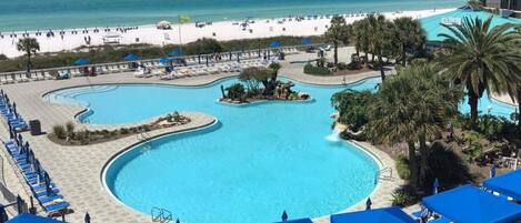 A resort with a large pool, beach, and palm trees.
