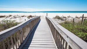 A wooden boardwalk leading to a beach with white sand and clear blue water.