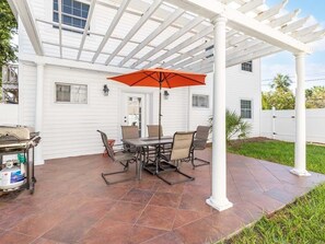 Une terrasse avec une table et des chaises, un parasol et un barbecue.