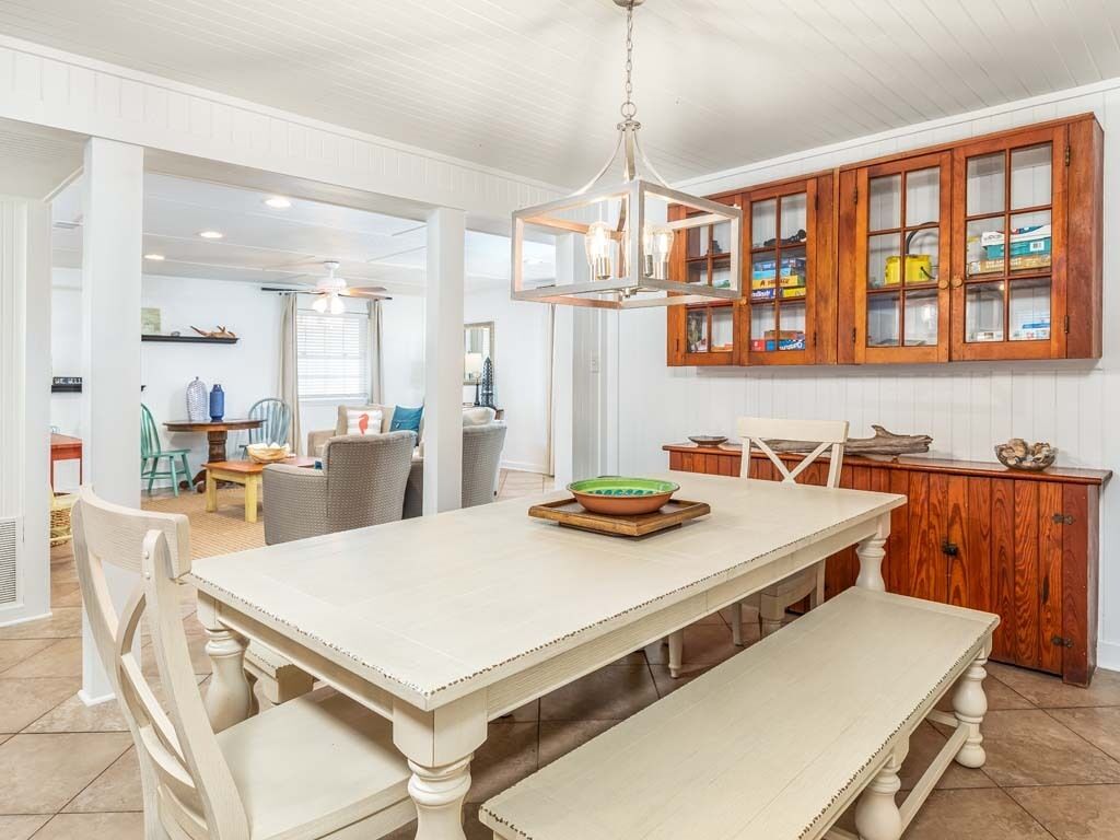Un coin repas avec une table et un banc blancs, des meubles en bois dotés de portes en verre et un luminaire suspendu.