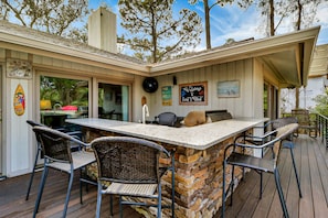 An outdoor bar area with a stone island, wicker chairs, and a grill.