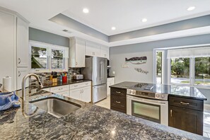 A modern kitchen with white cabinets, a granite countertop, stainless steel appliances, and a large window.
