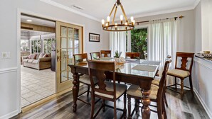 A dining area with a wooden table and chairs, a chandelier, and a view of a living room through a glass door. - Waterfront View Perfect for Fun Loving Families!  (Hilton Head Island)